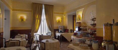A hotel dining area with round tables, chairs, and a buffet setup.