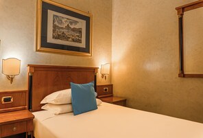 Una camera d'albergo con un letto, un comodino, una lampada a parete e un quadro incorniciato.