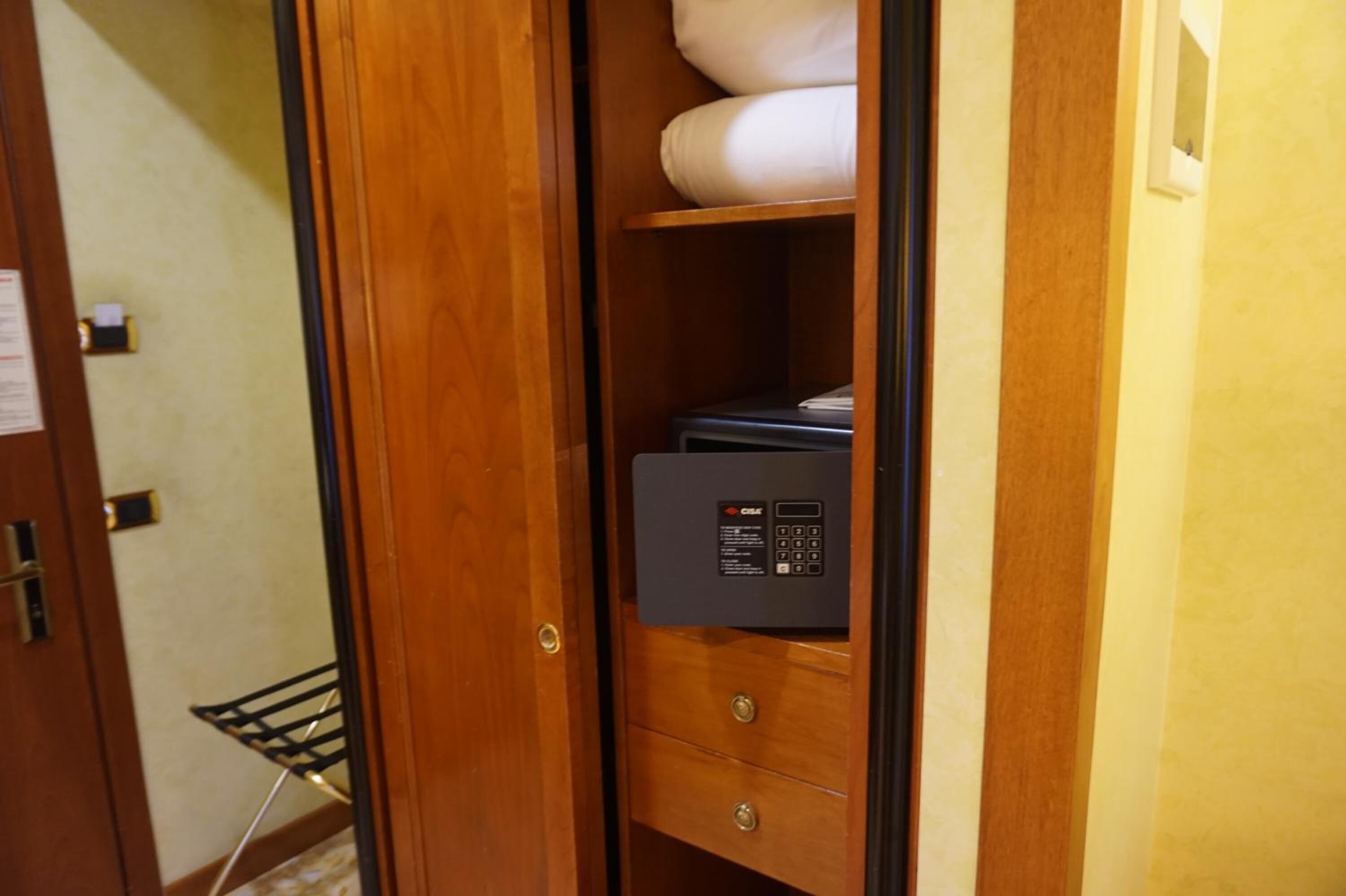Um guarda-roupa de madeira com painel de controlo embutido, barra para pendurar roupas e uma toalha branca dobrada.