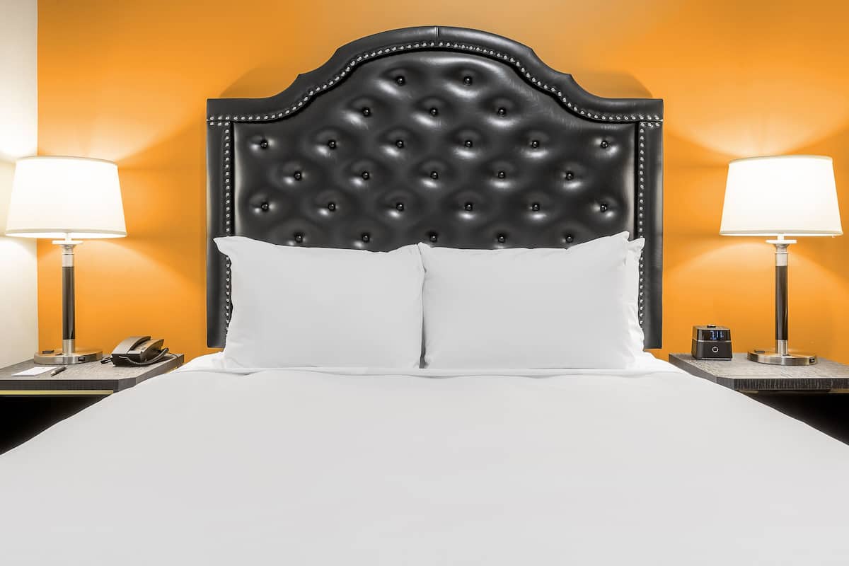 A hotel room with a tufted headboard, white bedding, two bedside tables with lamps, and a clock.