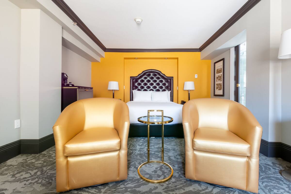 A hotel room with a bed, two chairs, a small table, and a lamp.