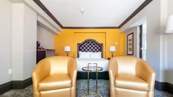 A hotel room with a bed, two chairs, a small table, and a lamp.