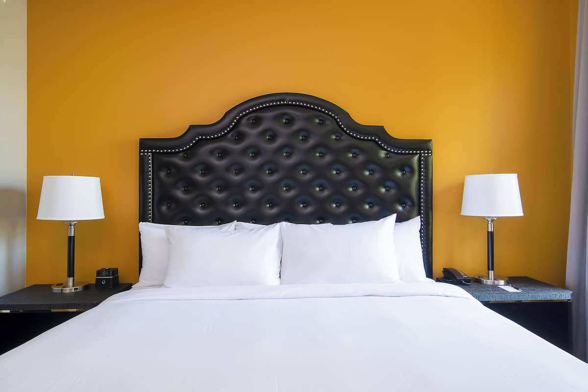 A neatly made bed with a tufted headboard, two bedside lamps, and a nightstand with a phone and a small clock.