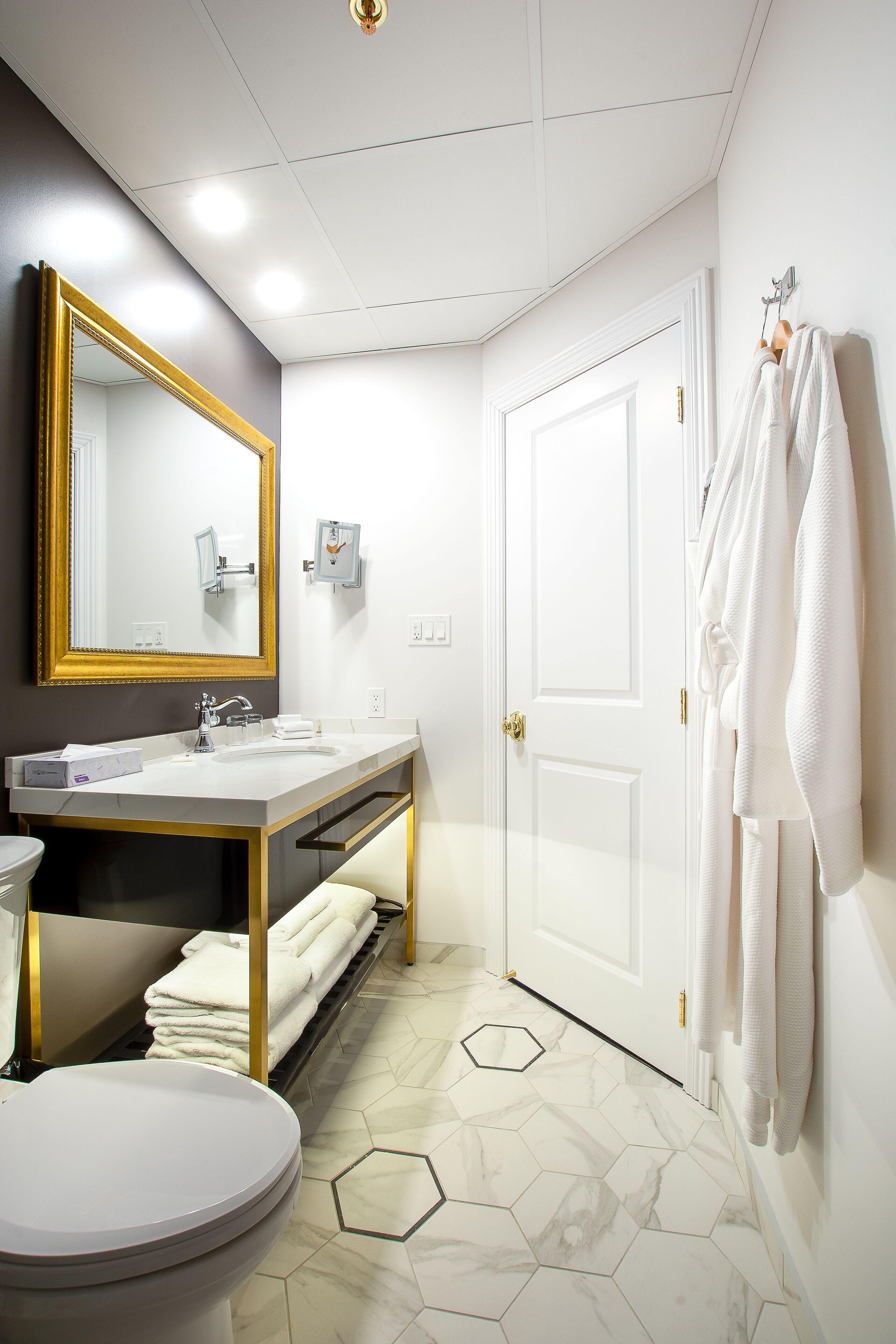 A modern bathroom with a white sink, gold fixtures, a large mirror, and a white toilet.