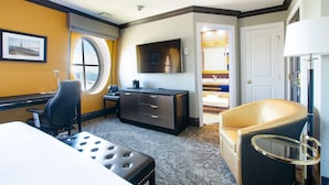 Quarto de hotel com cama, escrivaninha, cadeira, televisão e banheiro visível por uma porta aberta.
