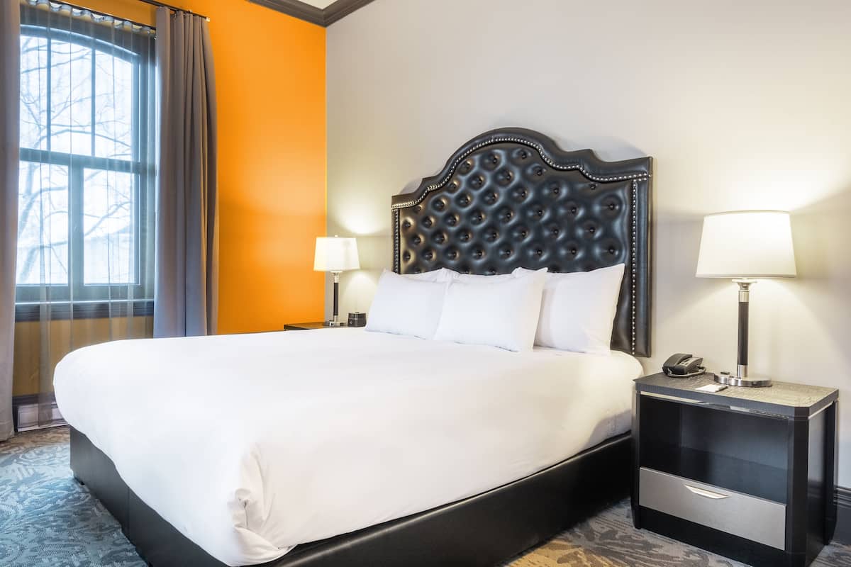 A hotel room with a large bed, a nightstand with a lamp, and a window with curtains.