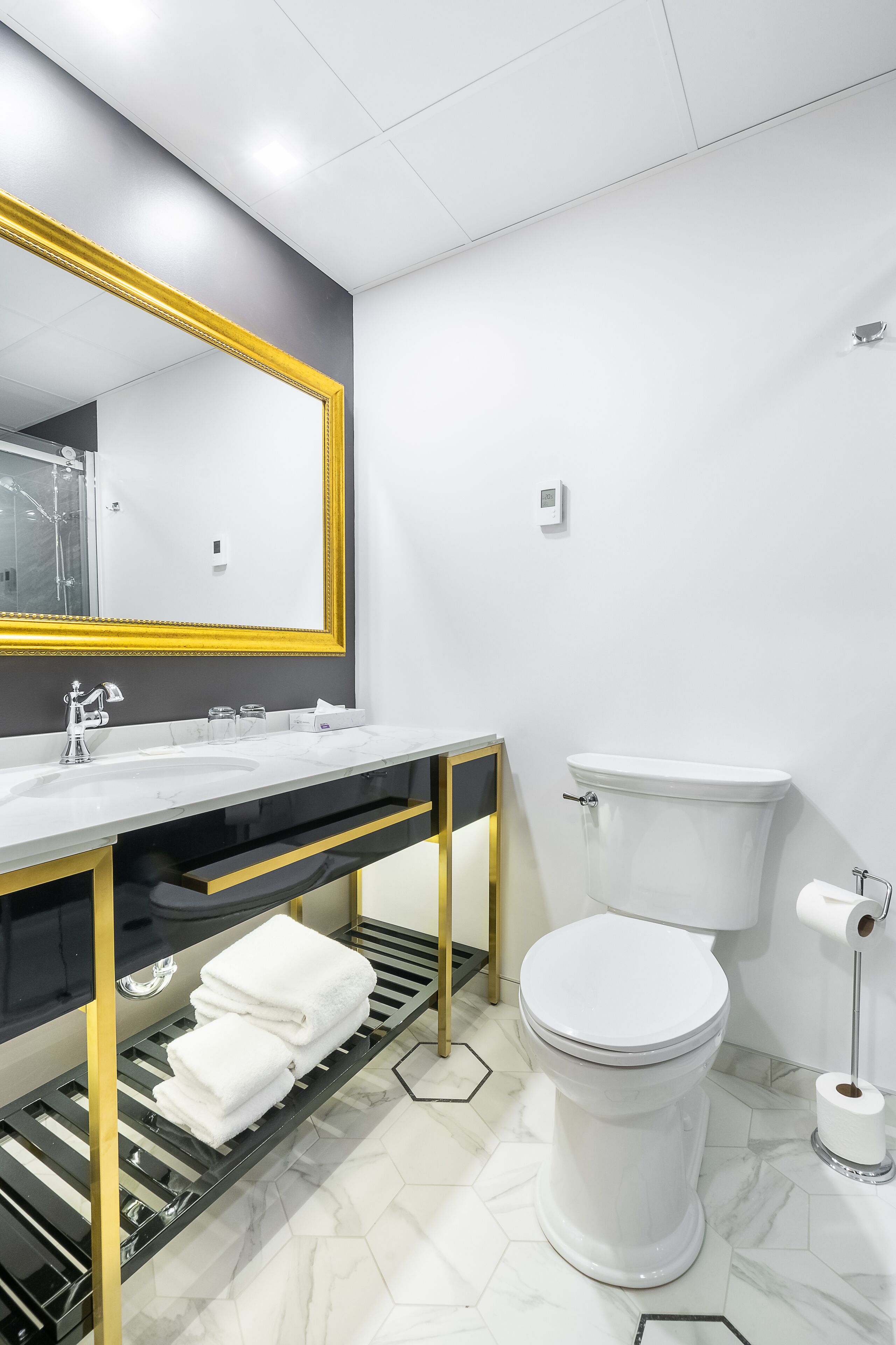 A modern bathroom with a white sink, gold-framed mirror, and a toilet.