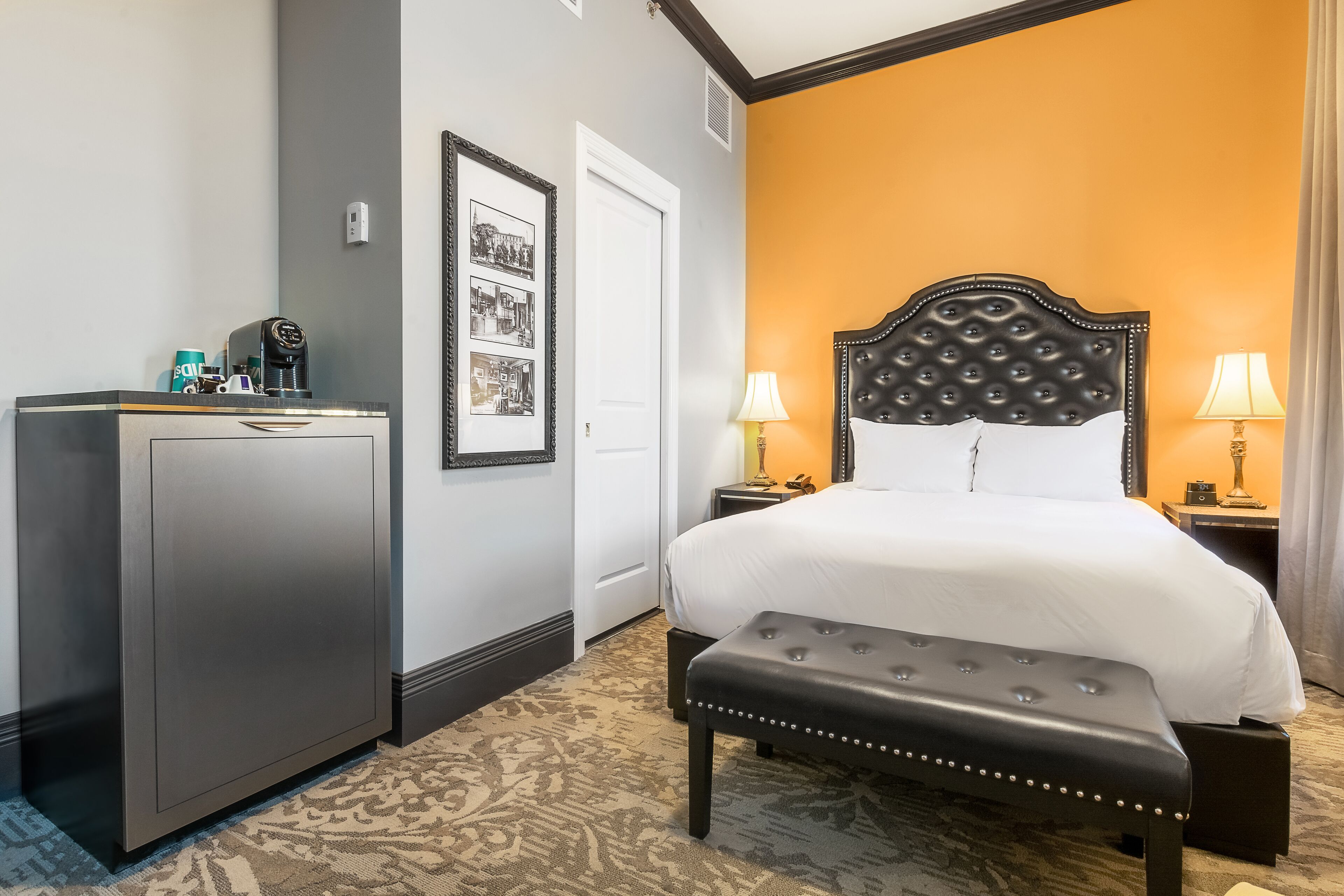 A hotel room with a bed, a desk, a bench, and a door.