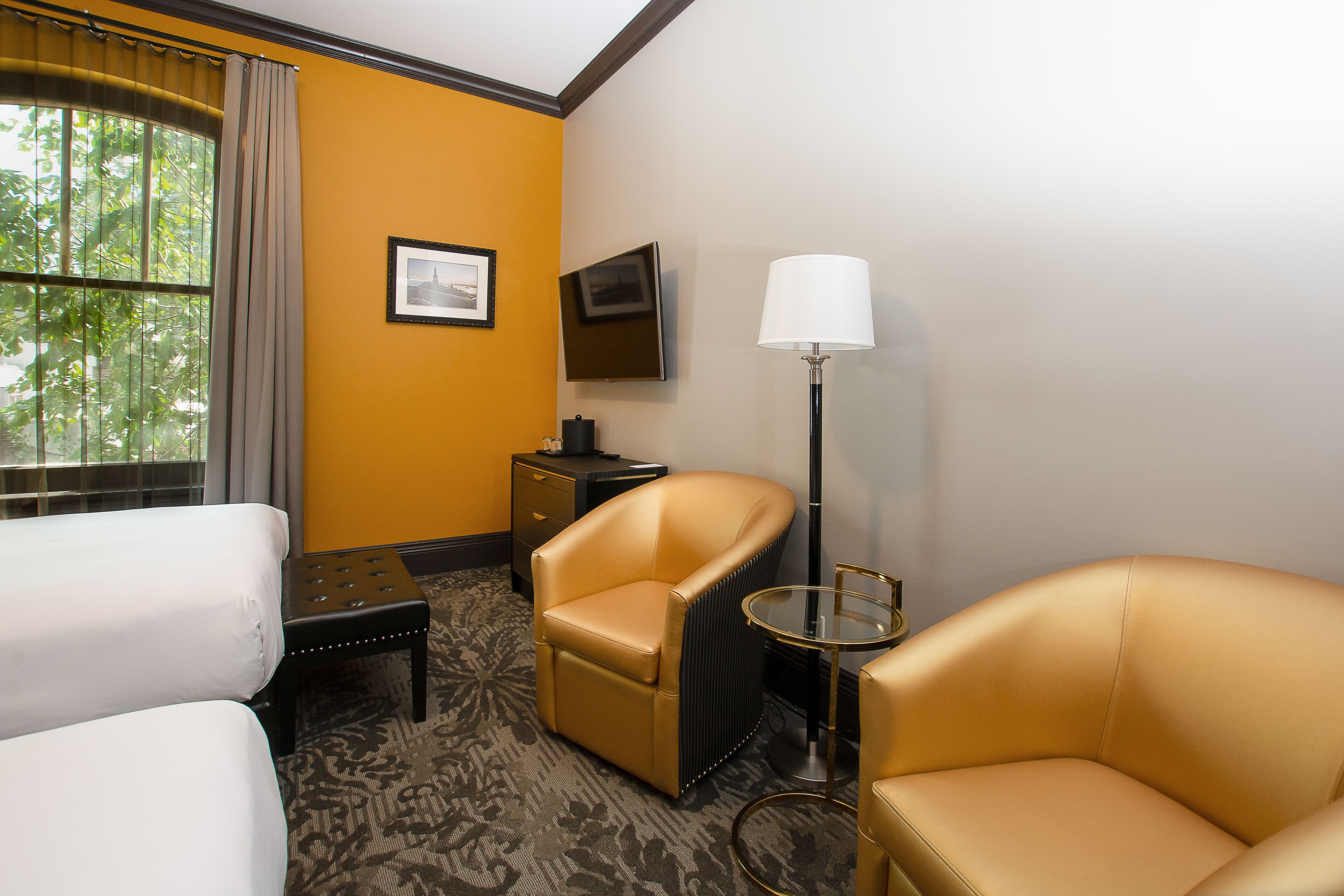 A hotel room with two beds, a sofa, a chair, a TV, a lamp, and a window with curtains.