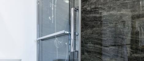 A modern bathroom with a glass-enclosed shower, a toilet, and a marble floor.