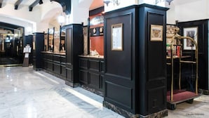Um hall com painéis pretos, piso de mármore e um espelho com moldura dourada.