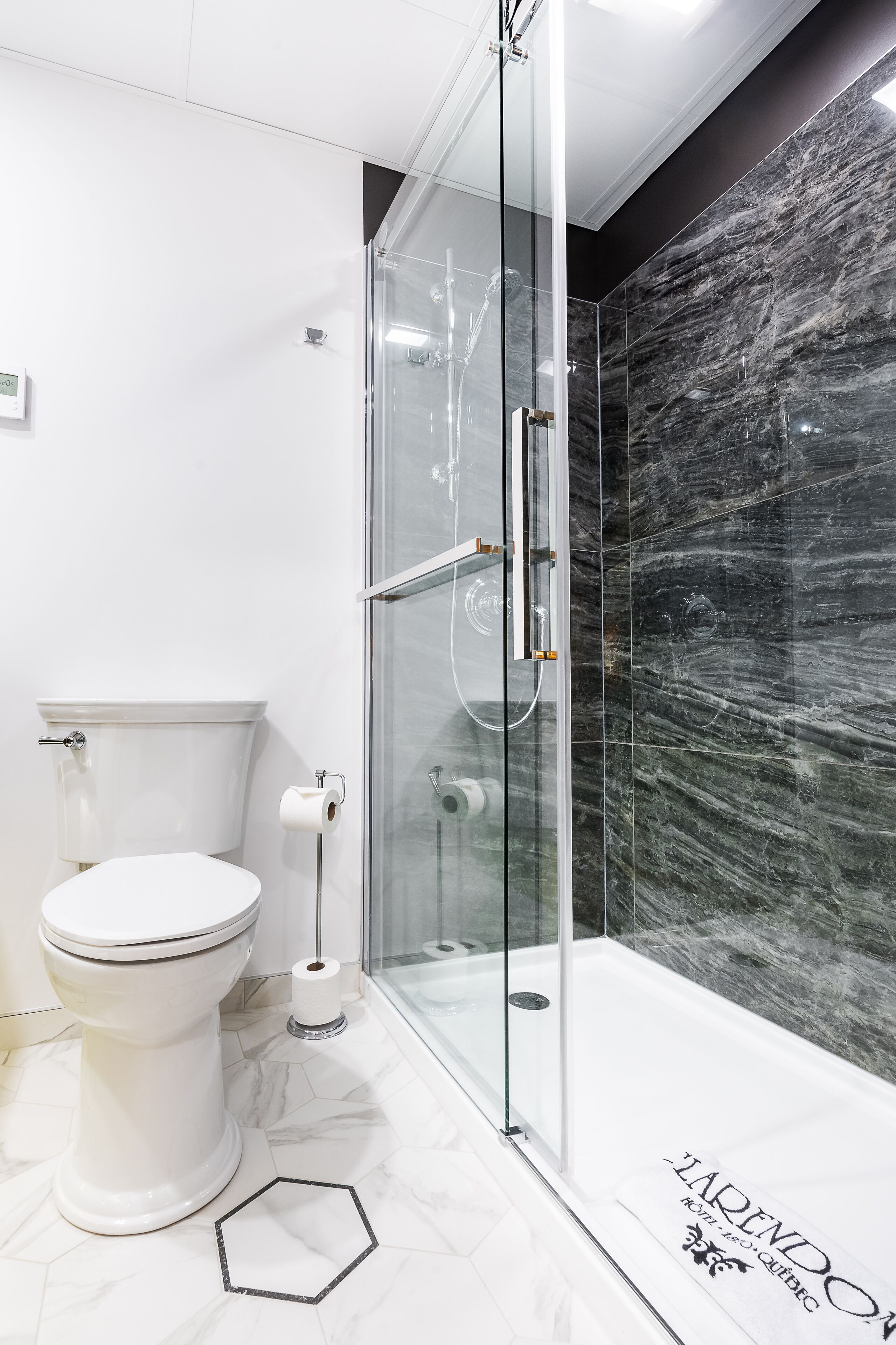 Un baño moderno con ducha acristalada, inodoro blanco y suelo de mármol.