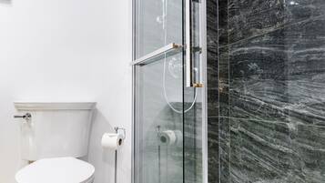Un baño moderno con ducha acristalada, inodoro blanco y suelo de mármol.