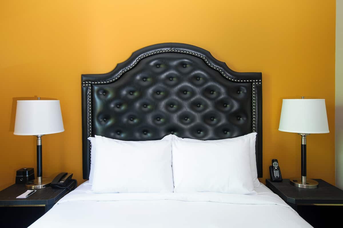 A hotel room with a tufted headboard, white bedding, two bedside tables with lamps, and a telephone on each table.