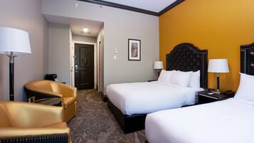 A hotel room with two beds, a sofa, and a desk with a lamp.