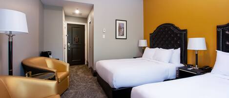 A hotel room with two beds, a sofa, and a desk with a lamp.