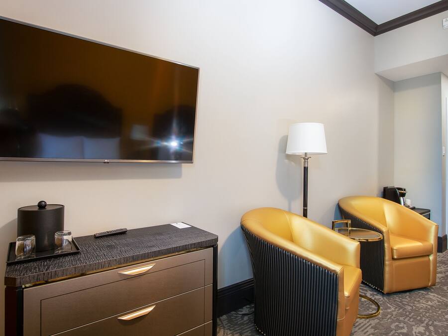 Een hotelkamer met een flatscreen televisie, een bureau met lamp, twee leren fauteuils en een minibar.