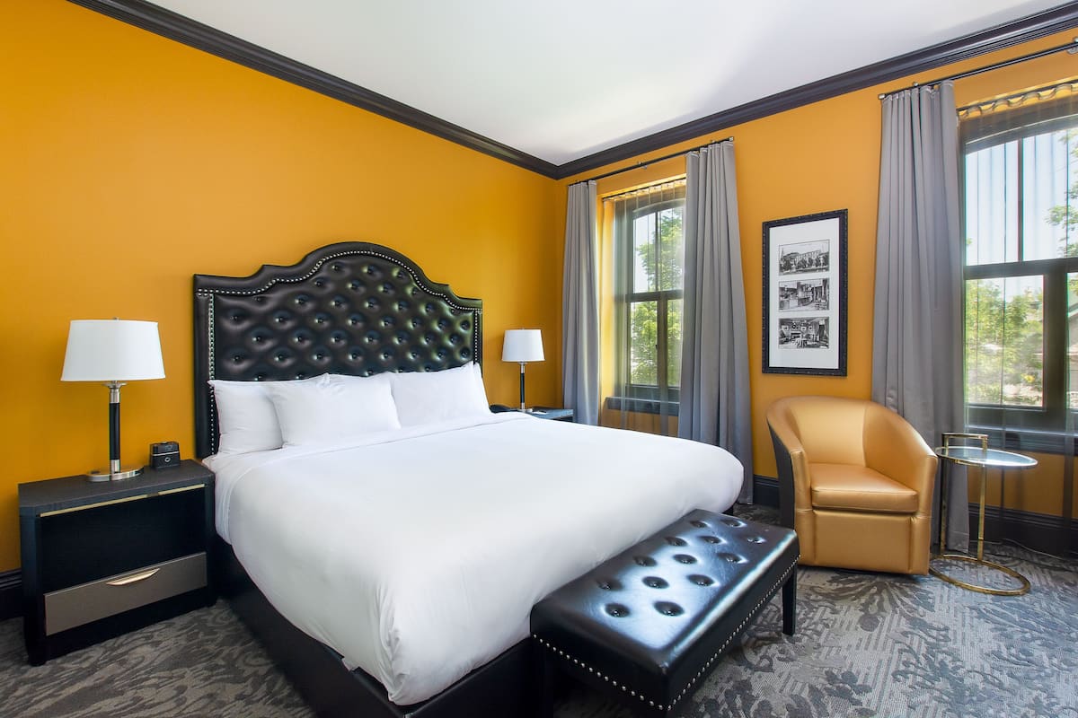 A hotel room with a large bed, a chair, a small table, and a nightstand.