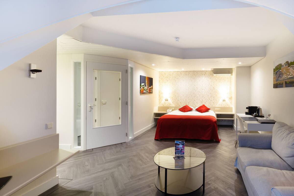 A modern hotel room with a bed, a sofa, a small table, and a TV.