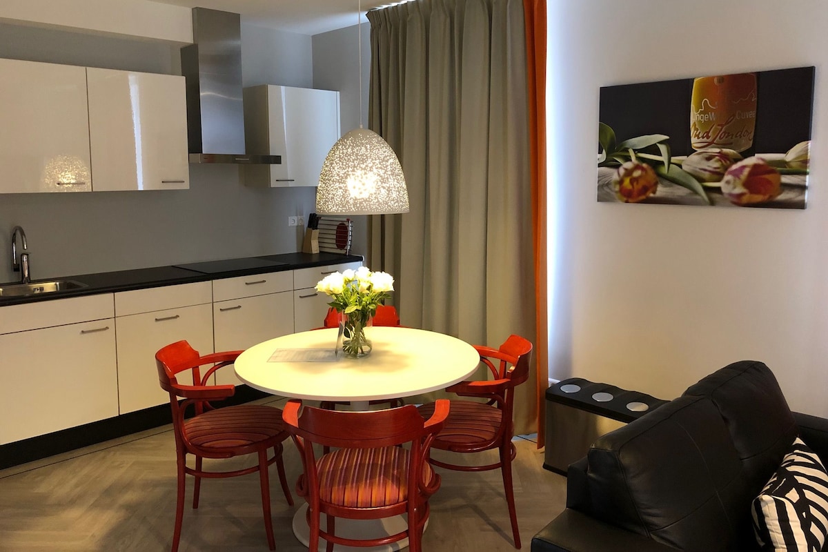 A modern kitchen with white cabinets, a round dining table with red chairs, a pendant light, and a painting on the wall.