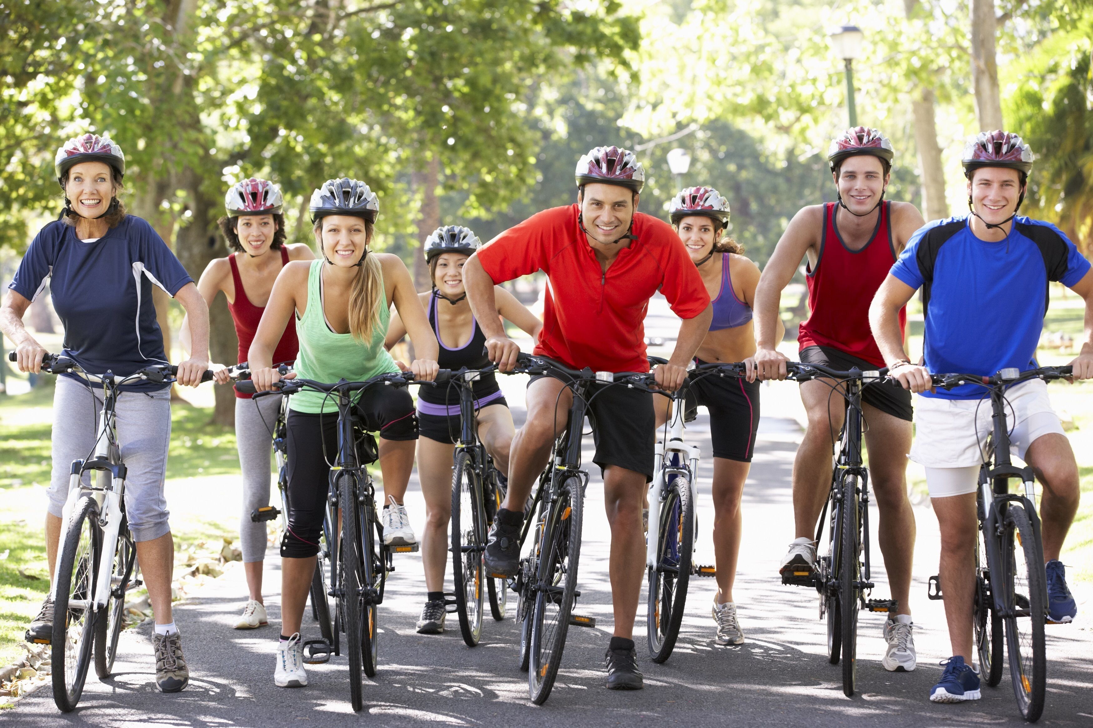 Un grupo de personas pedaleando en bicicleta por un camino pavimentado en un parque.