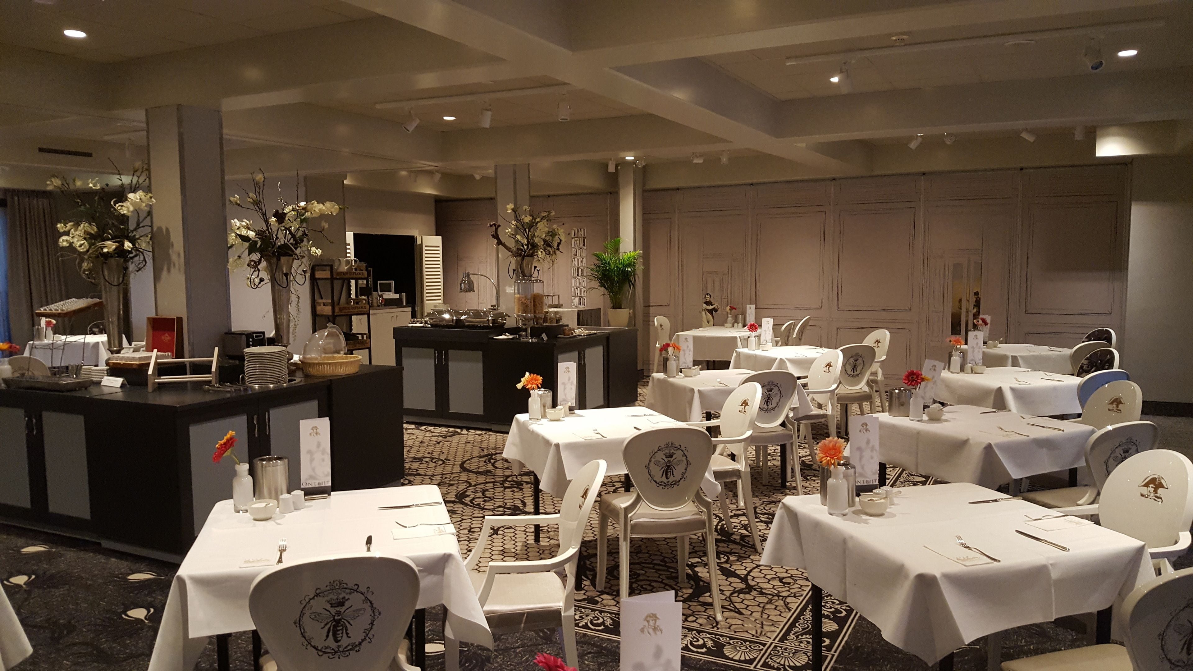 Un restaurante con varias mesas y sillas, una zona de bar y plantas decorativas.