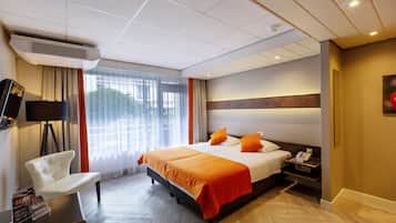 Una habitación de hotel con cama, escritorio, silla, televisor y ventana con cortinas.