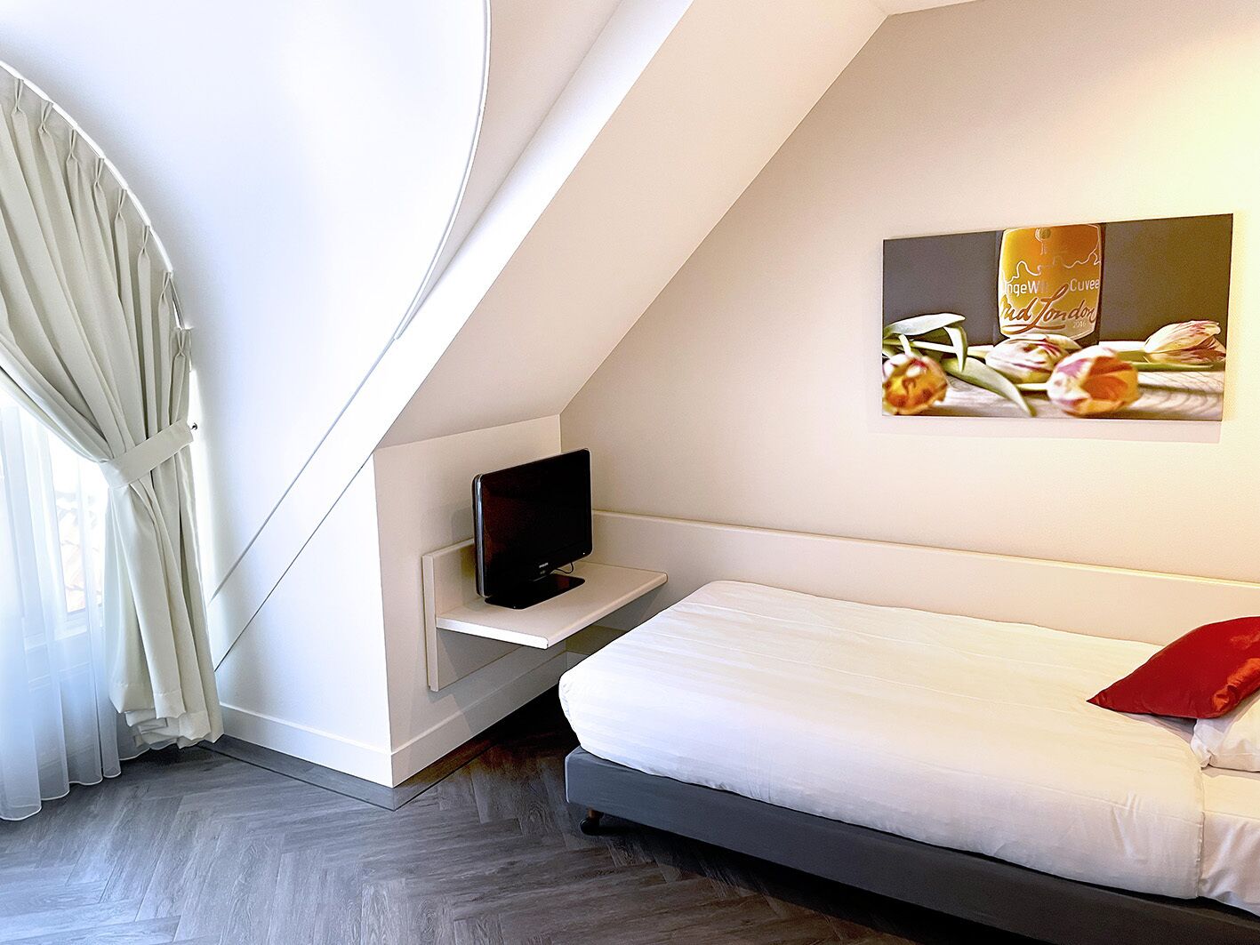 A modern bedroom with a bed, a TV on a shelf, and a painting of flowers on the wall.