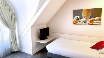 A modern bedroom with a bed, a TV on a shelf, and a painting of flowers on the wall.