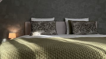 Un dormitorio con pared de estampado geométrico, cama con manta verde texturizada y dos almohadas con diseño de hojas.
