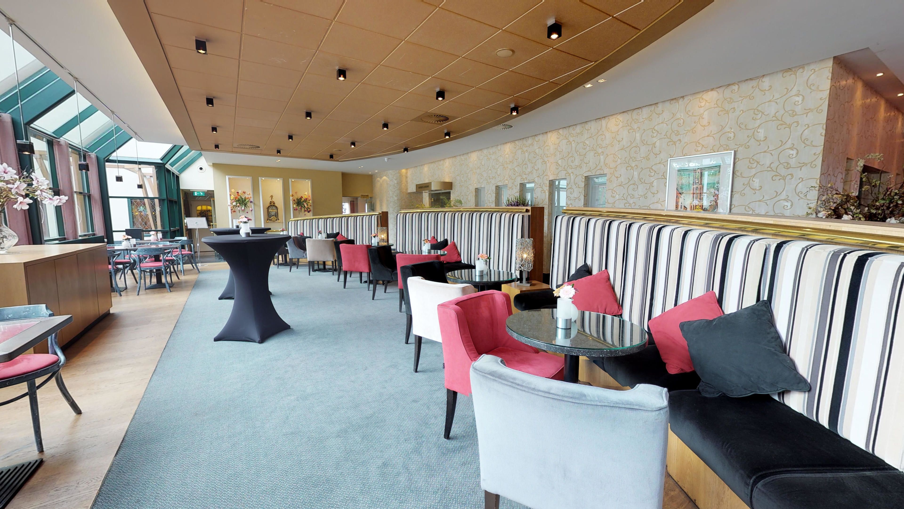 A spacious indoor area with seating arrangements, including round tables and cushioned benches, and a high ceiling with recessed lighting.