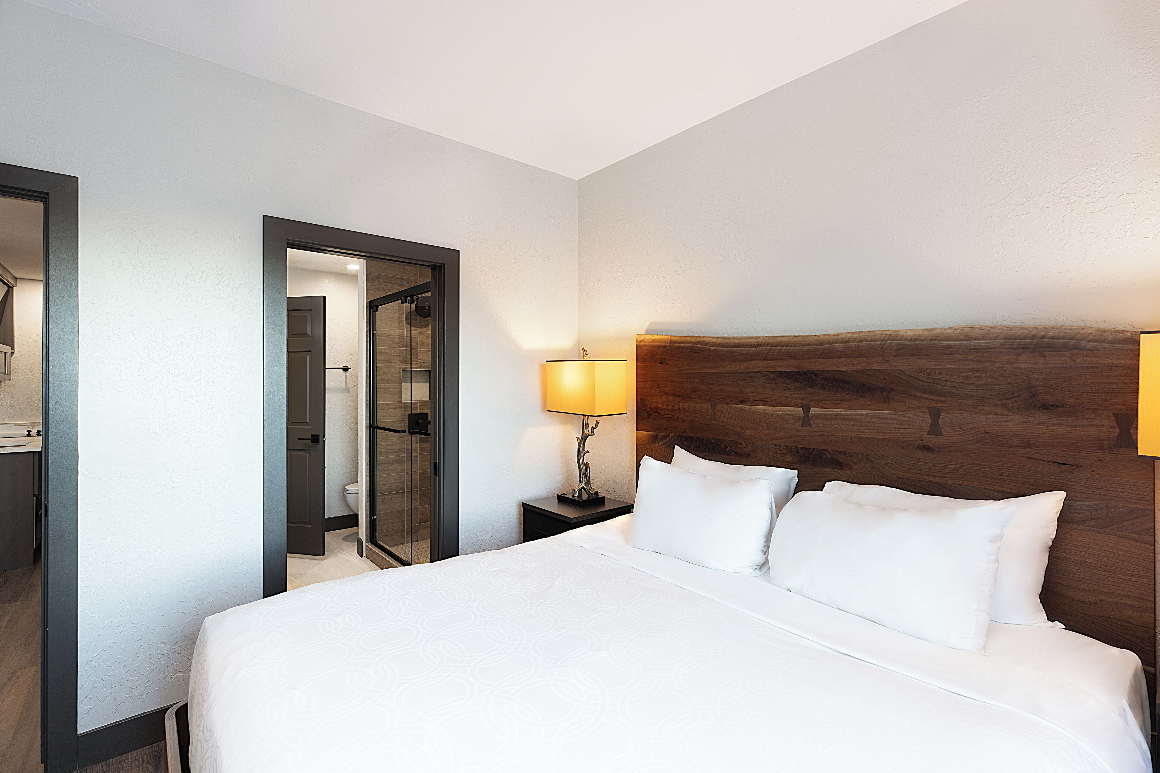 Ein Hotelzimmer mit einem großen Bett, einem hölzernen Kopfteil, einem Nachttisch mit Lampe und einem Spiegel an der Wand.