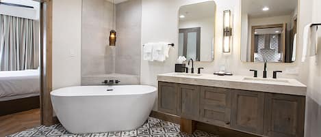 A modern bathroom with a freestanding bathtub, a vanity with a mirror, and patterned floor tiles.