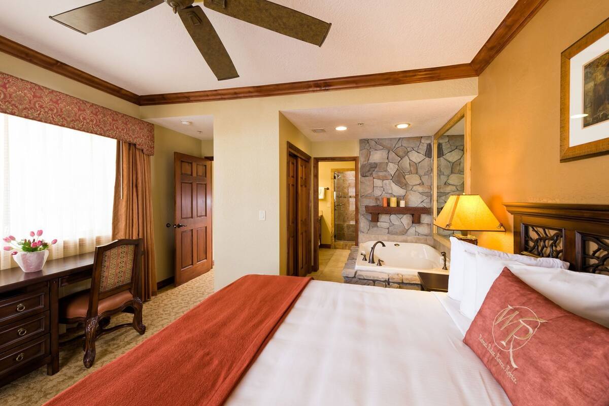 Habitación de hotel con cama, escritorio, silla, baño con bañera y pared de piedra.