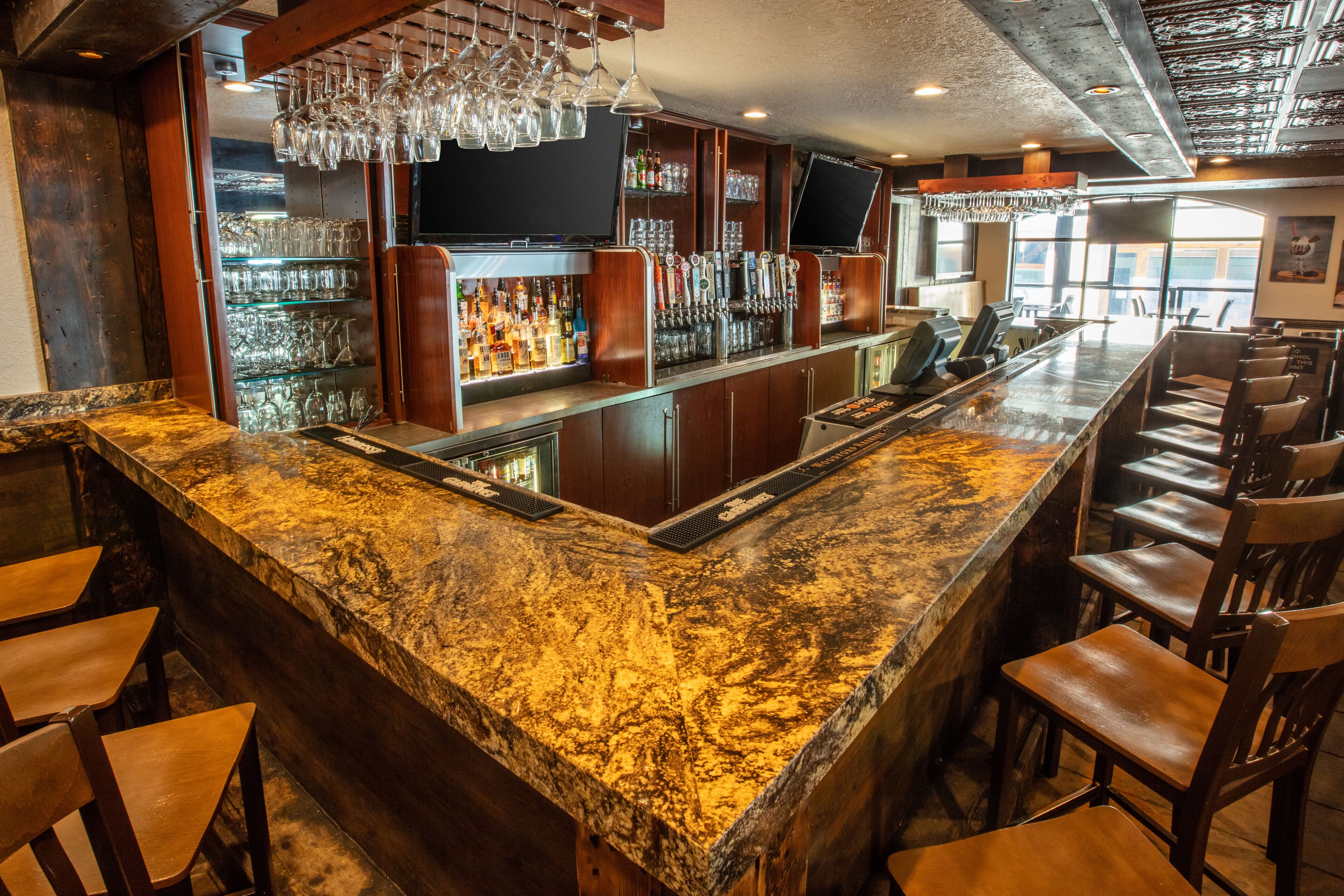 Una zona de bar con mostrador de granito, taburetes, un televisor y un enfriador de vino.