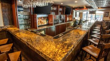 Una zona de bar con mostrador de granito, taburetes, un televisor y un enfriador de vino.