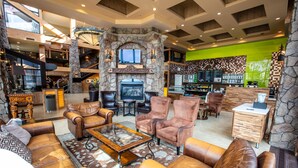 A spacious lobby with leather sofas, a stone fireplace, a bar area, and a staircase.