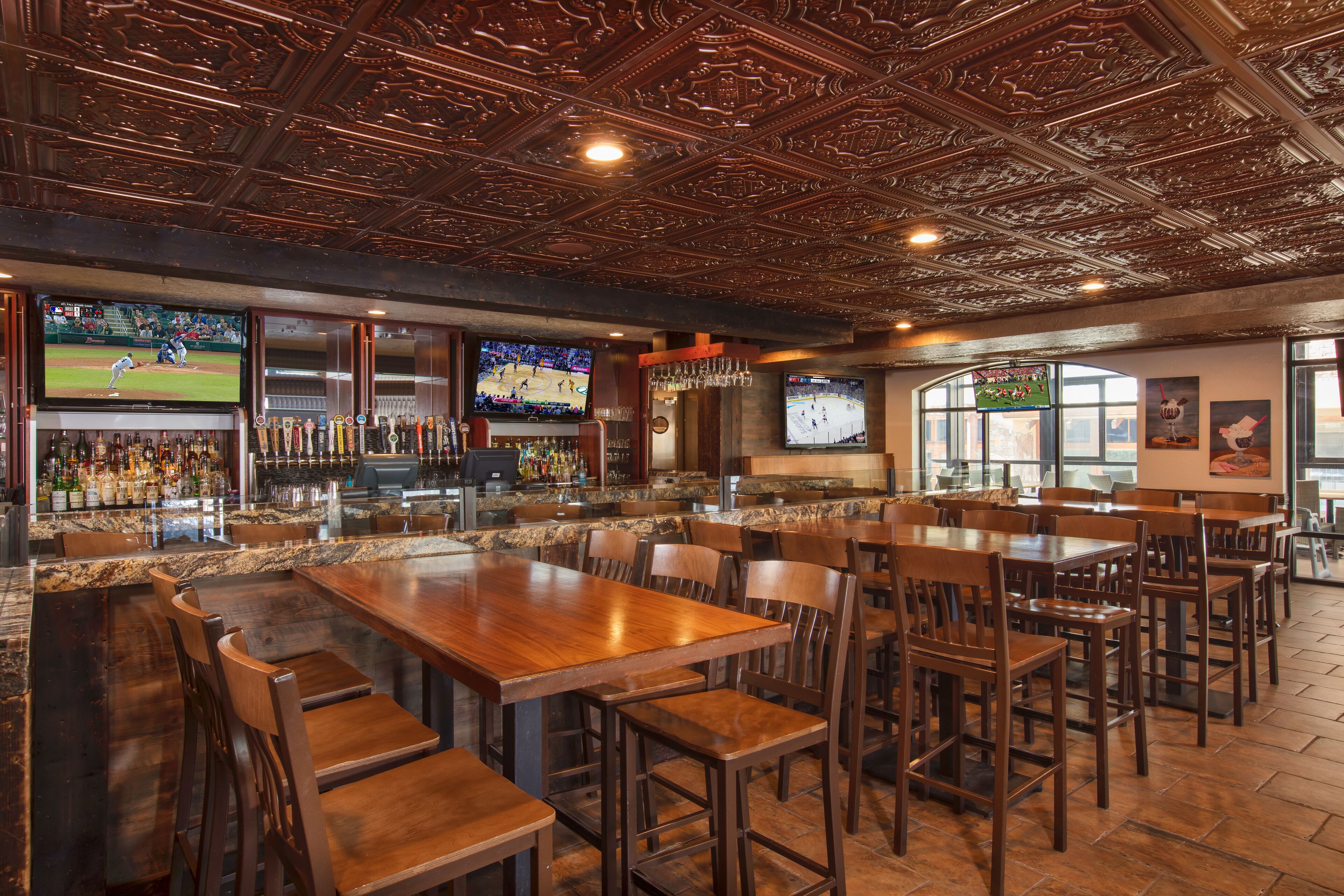 A bar area with multiple seating arrangements, a television displaying sports, and a bar counter with various bottles.