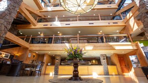 A multi-level lobby with wooden beams, stone accents, and a central round table with a floral arrangement.