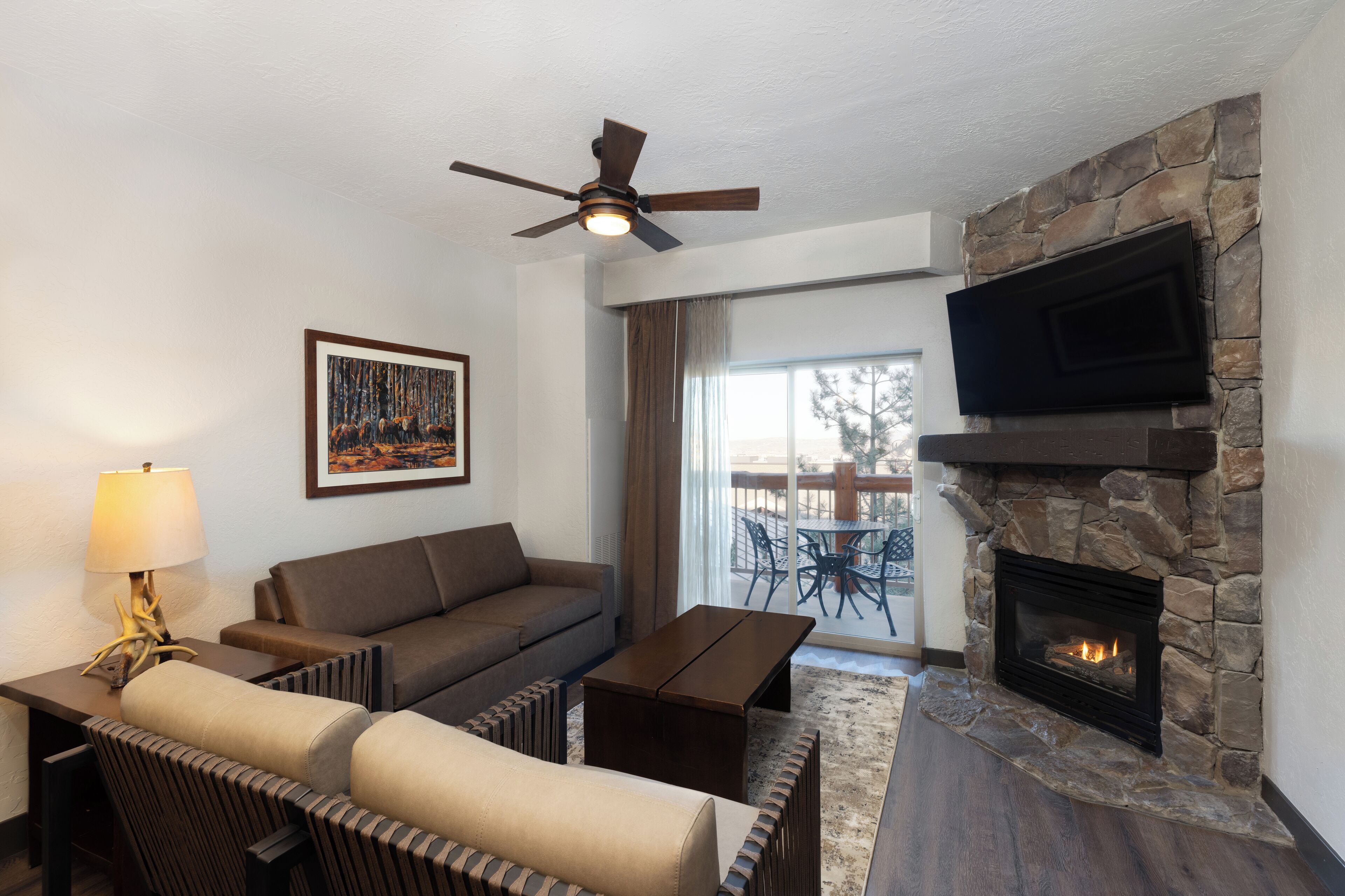 A living room with a stone fireplace, a ceiling fan, a sofa, a coffee table, and a TV mounted on the wall.