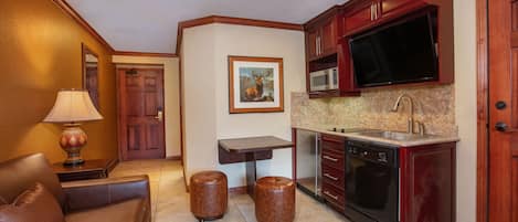 A compact kitchen with a microwave, stove, and sink. There is a wooden cabinet and a framed picture on the wall.