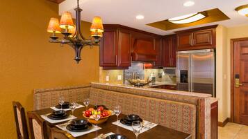 A dining area with a table set for four, a chandelier, and a kitchen with wooden cabinets and stainless steel appliances.