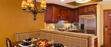A dining area with a table set for four, a chandelier, and a kitchen with wooden cabinets and stainless steel appliances.