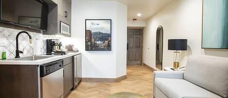 Una cocina moderna con lavavajillas, cafetera y lavabo. Hay un cuadro enmarcado en la pared y un sofá en la sala de estar.