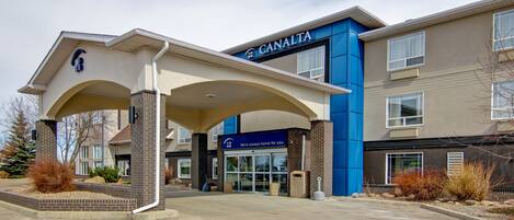 A CANALTA hotel entrance with a covered walkway, a blue and beige facade, and a clear sky.