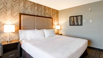 Una habitación de hotel con una cama grande, dos mesitas de noche con lámparas, un cabecero de madera, un revestimiento de pared con diseño de espiga y un cuadro enmarcado en la pared.