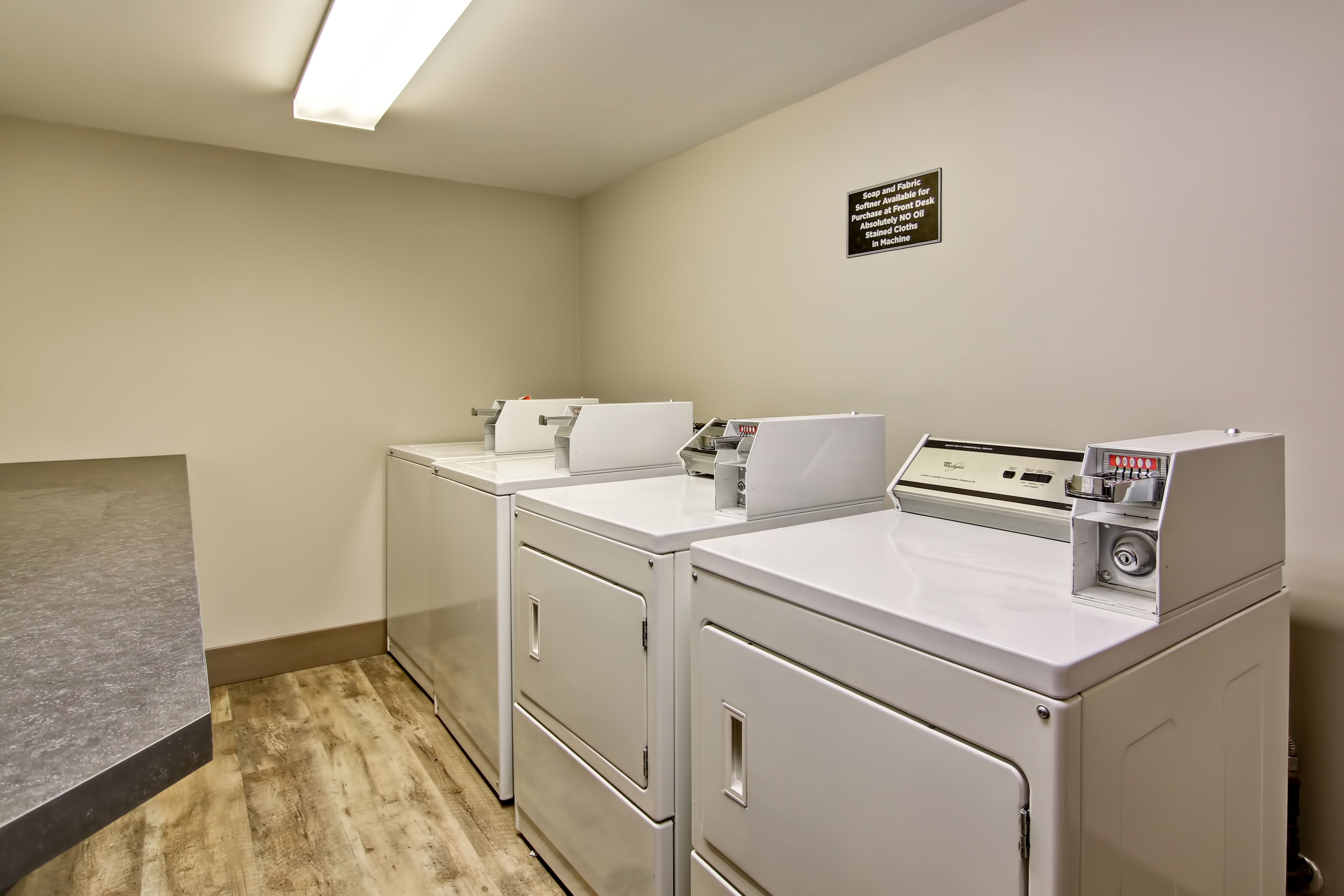 A laundry area with two front-loading washers and dryers, a sign indicating the use of fabric softener, and a gray countertop.