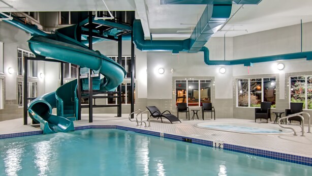 An indoor swimming pool with a spiral water slide and lounge chairs around the pool area. - Canalta Hotel Brooks (Brooks)