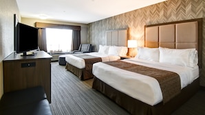 A hotel room with two beds, a desk with a TV, a chair, and a large window with curtains. - Canalta Hotel Brooks (Brooks)