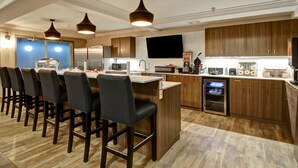 A modern kitchen with wooden cabinets, a central island with bar stools, a built-in oven, and a flat-screen TV. - Canalta Hotel Brooks (Brooks)